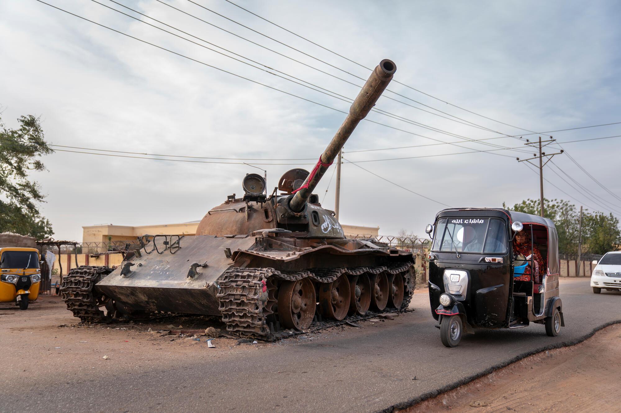 Un taxi rickshaw contourne un char détruit appartenant aux forces armées soudanaises, vestige des violents affrontements qui ont eu lieu à El Geneina en 2023. Darfour occidental, Soudan, février 2024. © Diana Zeyneb Alhindawi